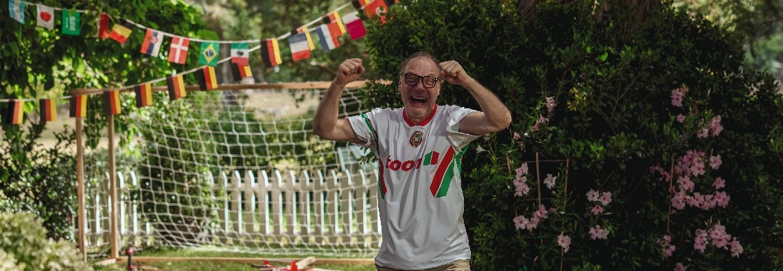 Eine Person jubelt im Garten vor einem Fußballtor.